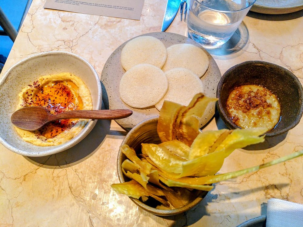 Sinasir Rice Pancake w/ Black-eyed Bean Hummus
"Sinasir: a Northern Nigerian rice pancake with a fluffy texture and subtle nutty undertones"

Green Plantain Chips w/ Aubergine Yassa
"Aubergine Yassa: A twist on the Senegalese classic, roasted aubergines gently folded into a rich, tangy-sweet yassa sauce of slow-caramelised onions, and bright citrus."