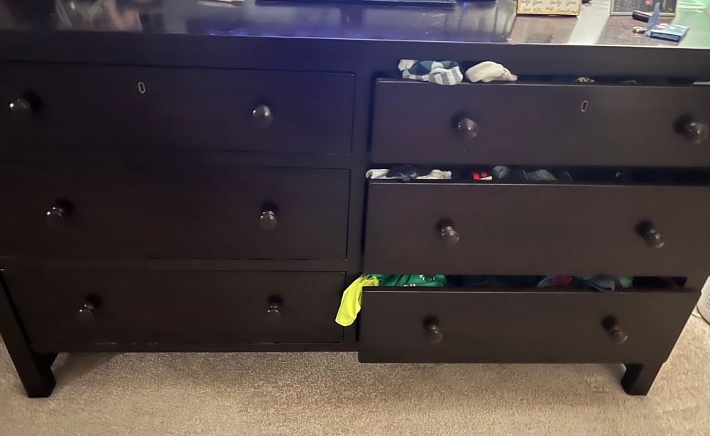 Two sets of drawers side by side. On one side all drawers are nearly closed, and on the other all the drawers are open with clothes spilling out. 
