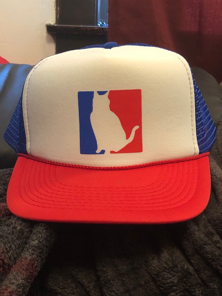A red, white, and blue trucker hat with the NBA logo redesigned with a cat instead of Jerry West’s silhouette 