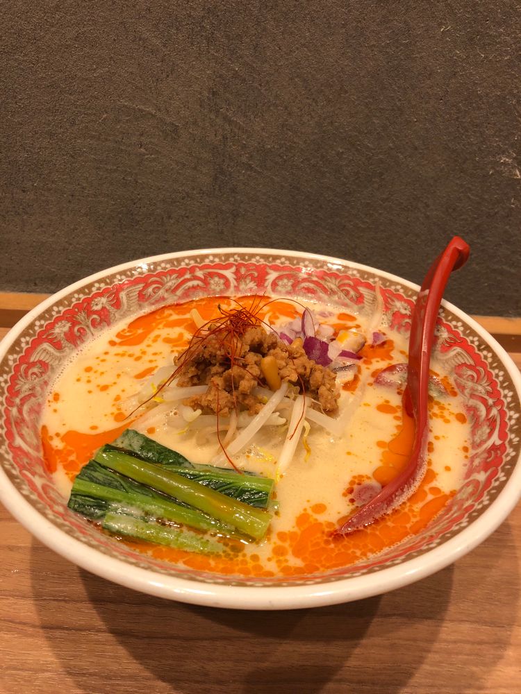 A red porcelain bowl filled with vegan tantan noodles topped with moyashi, chingensai and soy mince. 