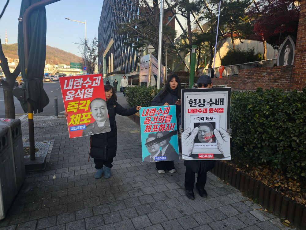 Three South Korean residents in Seoul hold signs calling for the arrest of President Yoon Suk Yeol, who declared martial law last week. 