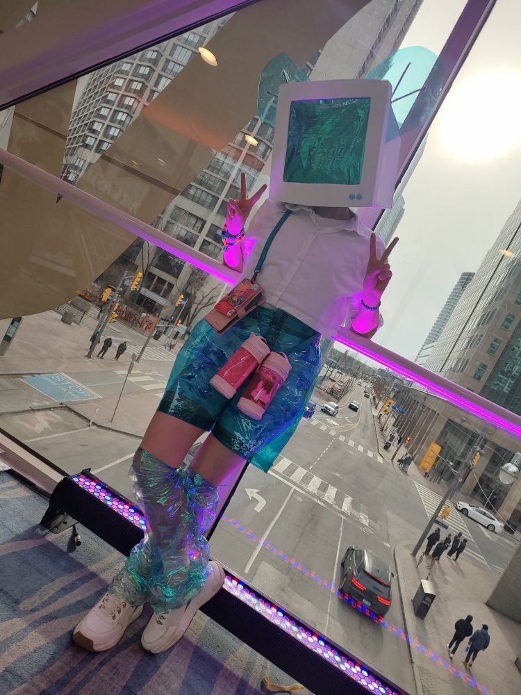 The user's fursona (a computer head with transparent blue mouse ears) posed giving the peace sign on the skybridge at Furnal Equinox 2025. 