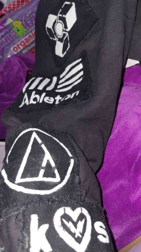 Black jacket with DIY patches of Ableton, Audio Technica, Kilohearts, and  Reason.