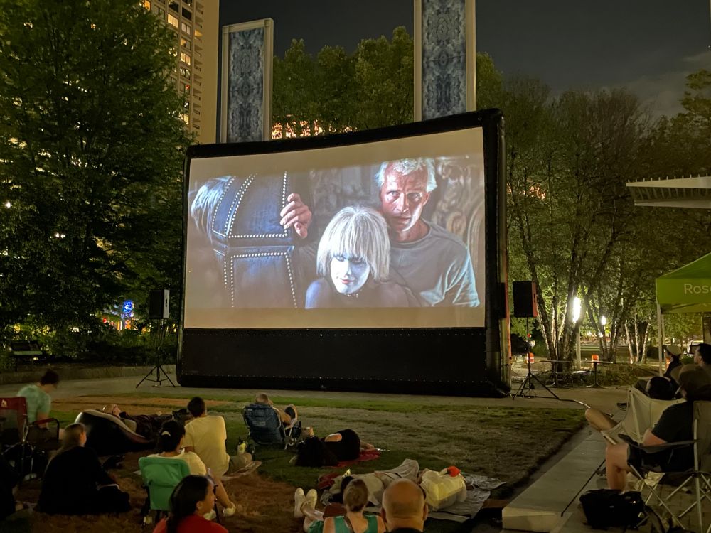 Shot of Roy and Pris in Blade Runner, which is playing on an outdoor screen during the evening.