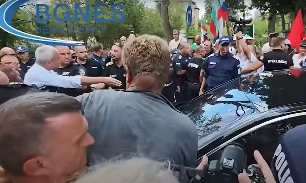 Von der Seite: Gedränge um schwarzen Audi, viel Polizei, vor dem Auto Kostadinov gestikulierend 