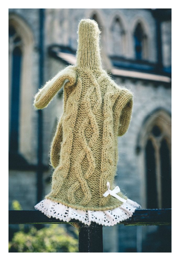 Close up of a single ornate knitted glove on the spike of some railings in front of a church. It looks like the glove is flipping the bird.