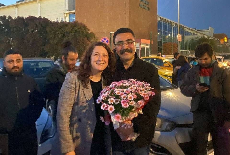 Fotoğrafta, Selçuk Kozağaçlı elinde pembe-beyaz çiçeklerden oluşan bir buket tutuyor. Yanında gülümseyen bir kadınla birlikte poz veriyor. Akşam saatlerinde, bir otopark alanında çekilmiş gibi görünen karede arka planda birkaç kişi ve arabalar var. Ortamda sıcak ve sevinçli bir hava hissediliyor.