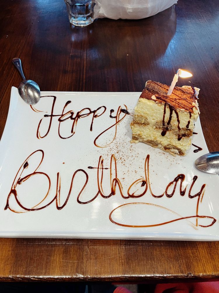 A large white plate with HAPPY BIRTHDAY written in chocolate with a piece of tiramisu to the side