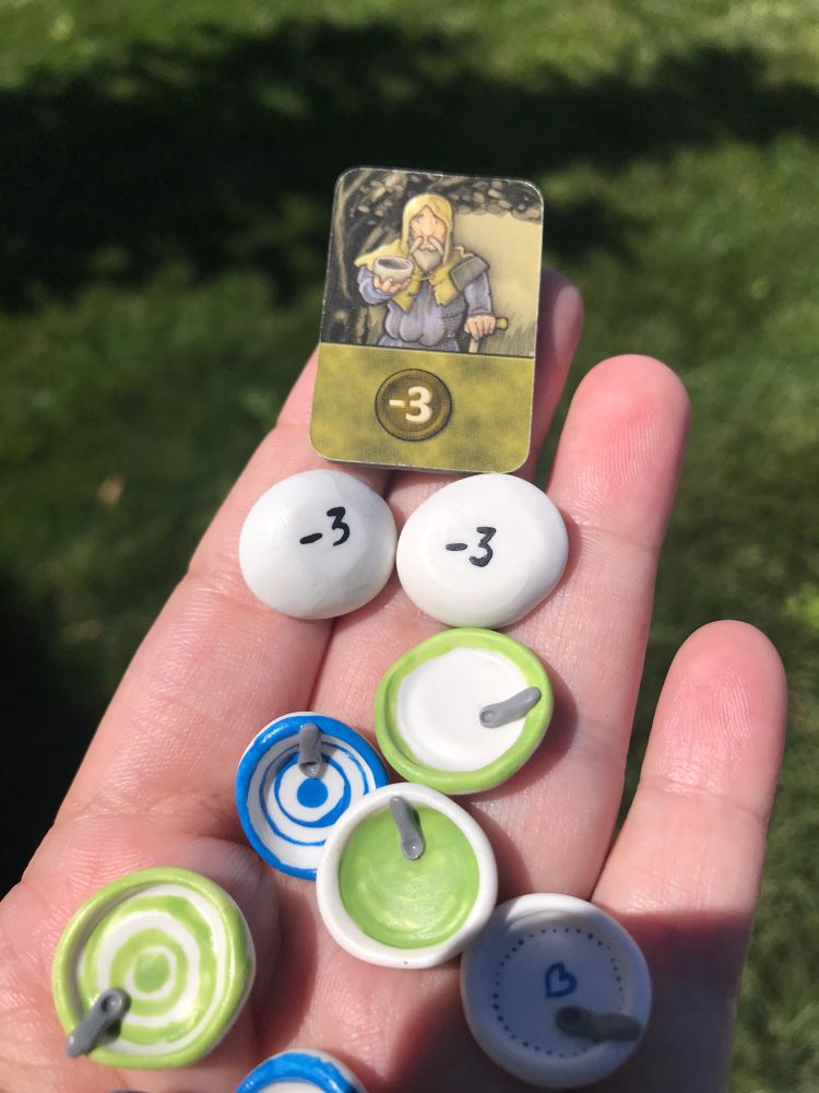 Colorful miniature hand painted bowls and spoon upgrades for the board game Agricola, shown alongside the original “beggar” token that the game comes with. This set of 10 bowls is painted with blue and green patterns, although in the future I may make a set that matches the player token colors. 