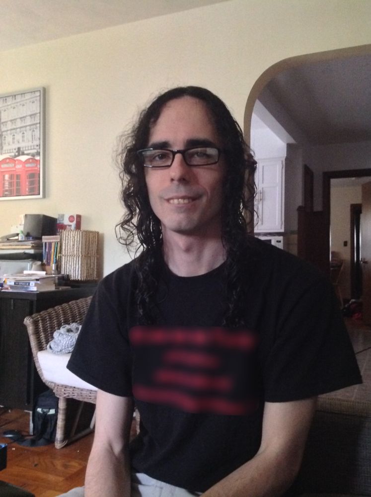 A picture of Sable, a pre-transition white woman, from 2016, wearing a black t-shirt with blurred red lettering. She's sitting and trying to smile but it does not reach her eyes. Her curly, center-parted black hair is quite long, but thin and scraggly, and her eyes look dead. Her eyebrows are huge and unkempt.

Notably, she's also alarmingly thin.