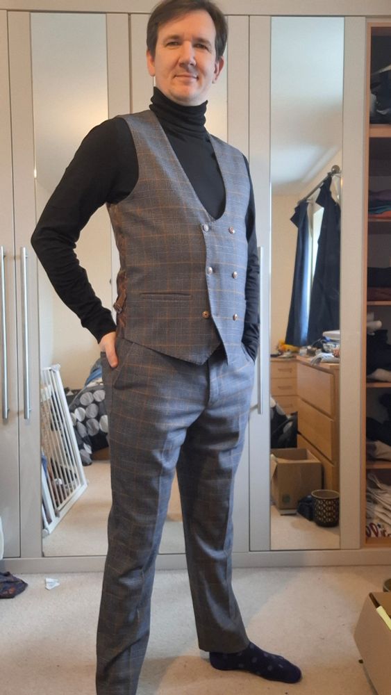 Selfie of me in matching pair of waistcoat and smart trousers, in a grey with burtnt orange gatch pattern, and a black turtleneck.
