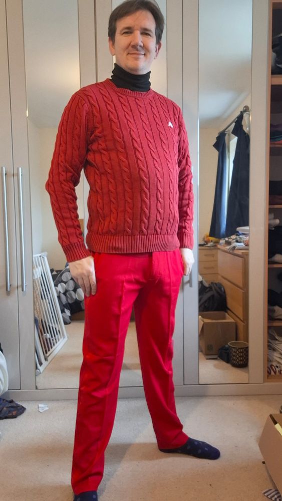 Selfie of me in bright red smart trousers, with a brown belt, a red jumper with chunky knit pattern, and a black turtleneck poking out the collar.