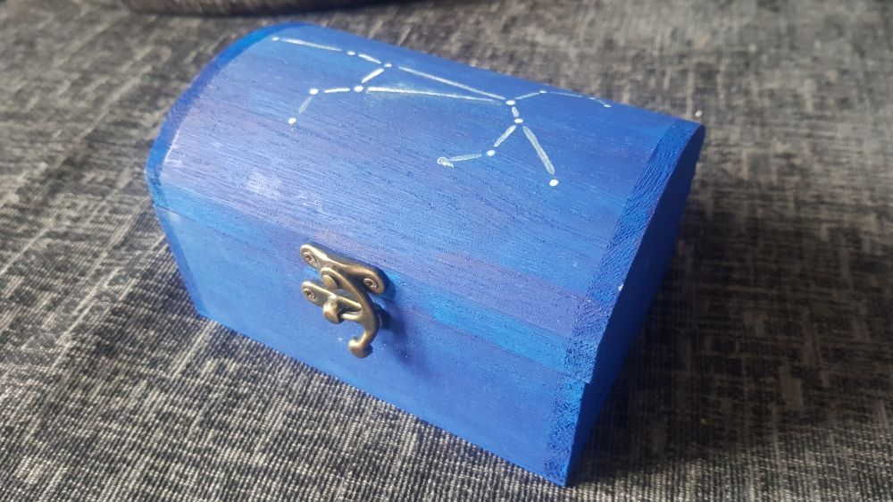 An angled shot of a closed treasure chest, painted blue, with a constellation of a white horse painted on top.