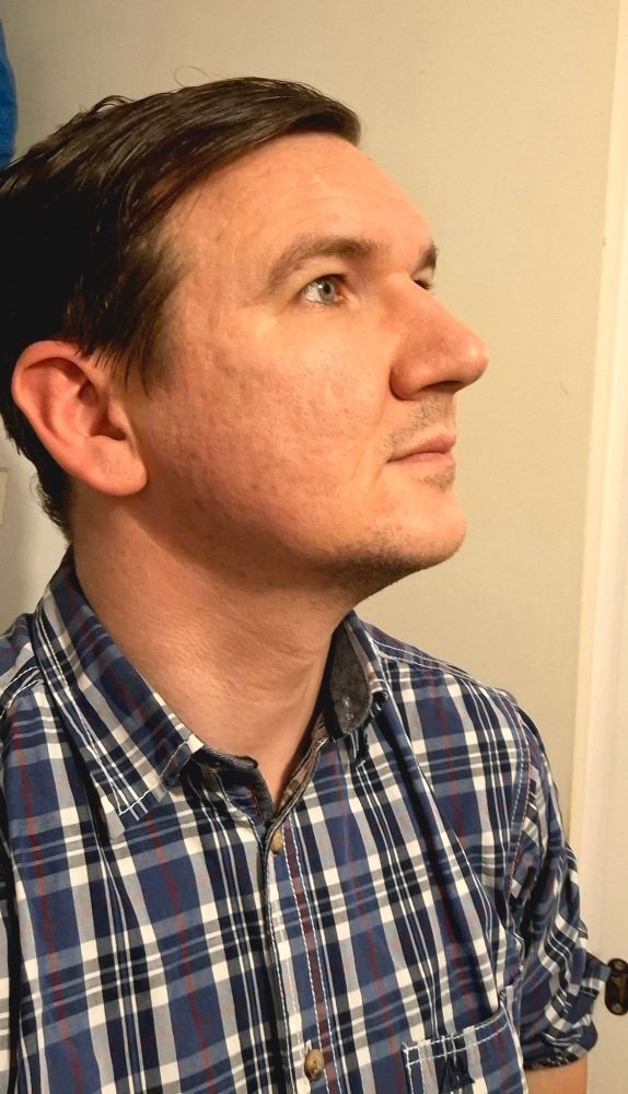 Selfie of me, a 41 year old white man, taken from a 45-degree side angle, as I look to the right of the photo. I'm in a rolled up shirt, with a blue and white checked pattern.