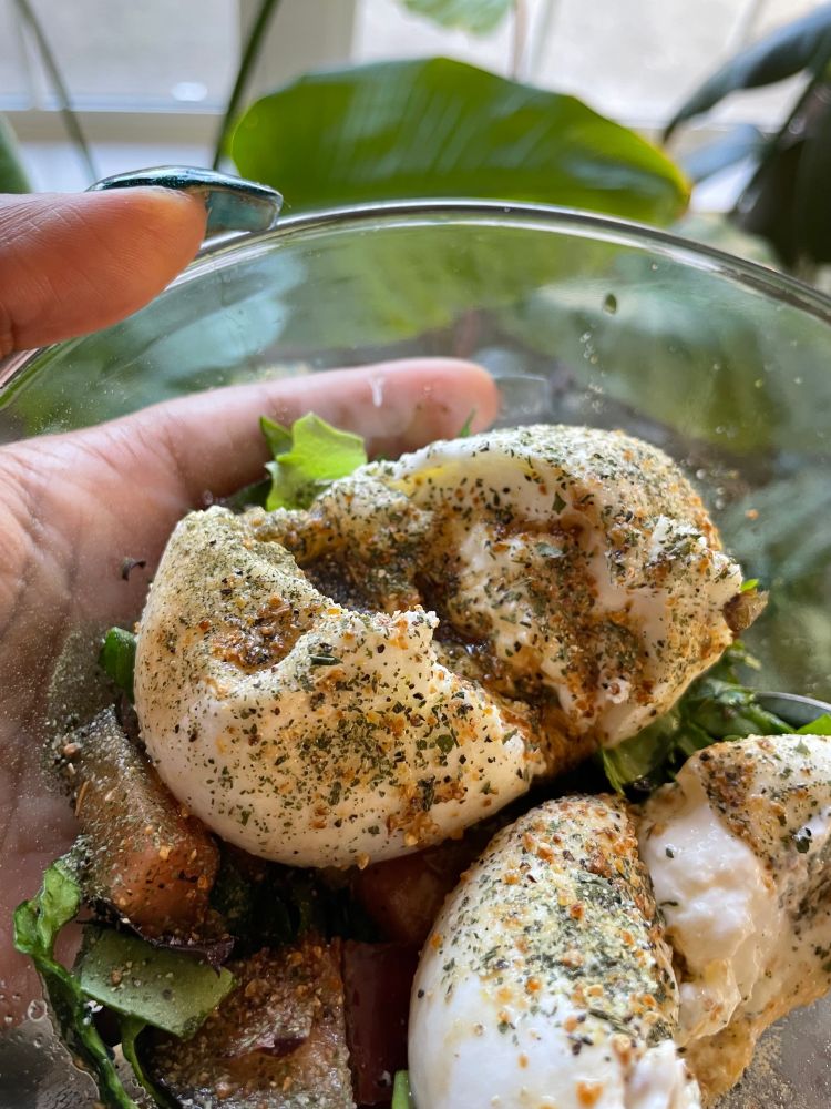 Burrata with balsamic vinegar, olive oil, basil, garlic powder, and salt & pepper in a glass bowl on top of spring mix lettuce and tomatoes.