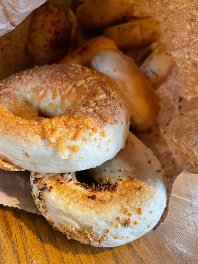 A paper bag filled with different flavors of bagels on a wooden table.