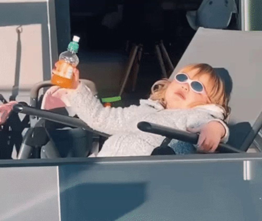 a little girl wearing sunglasses sits in a chair holding a bottle of orange juice