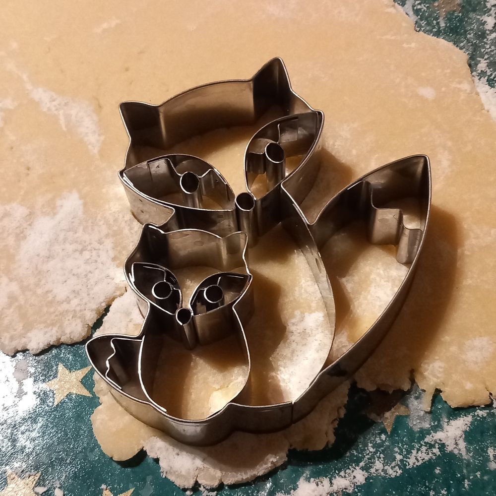 A cookie cutter of two foxes on rolled out cookie dough