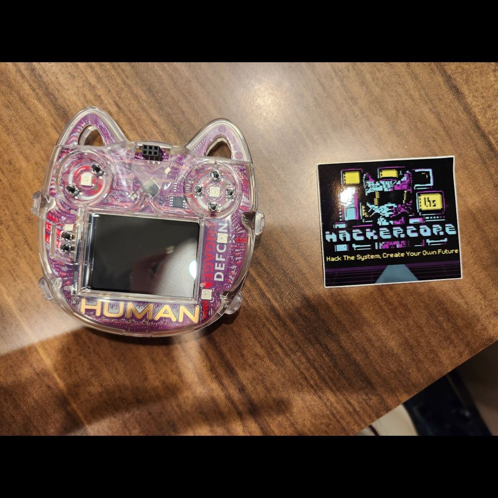 The aforementioned Hackercore sticker sits on a table next to a cat-head-shaped badge reader device. 