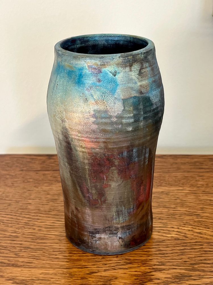 A slender vase gently flaring at the top, glazed in various hues with flashes of metallic copper, reds, and hints of blue. 