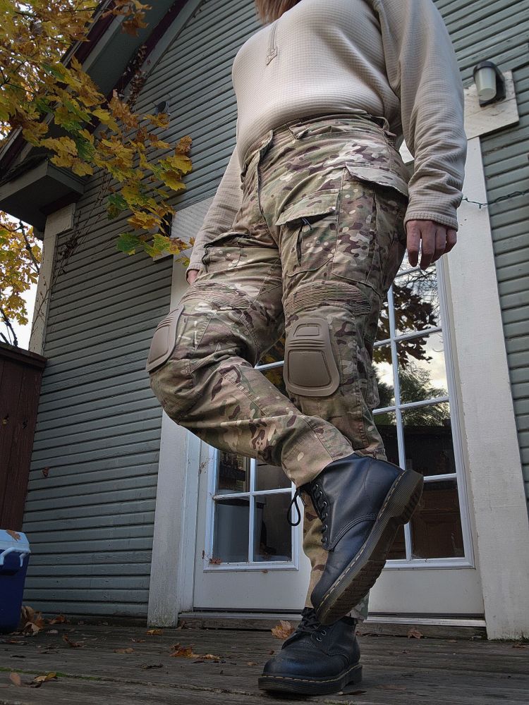 langley stands on one leg on a deck. she's wearing doc martin boots, multicam crye G3 clones, and a waffle top 