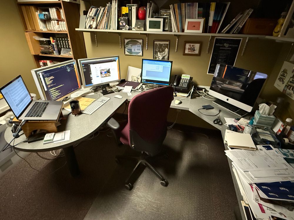 A desktop including a MacBook Pro with two Cinema Display Monitors. On showing VSCode, the other showing Wes Bos’ post. A Windows XP monitor with an old version of Crystal Reports displayed. And an older iMac that I’m afraid to turn on. 