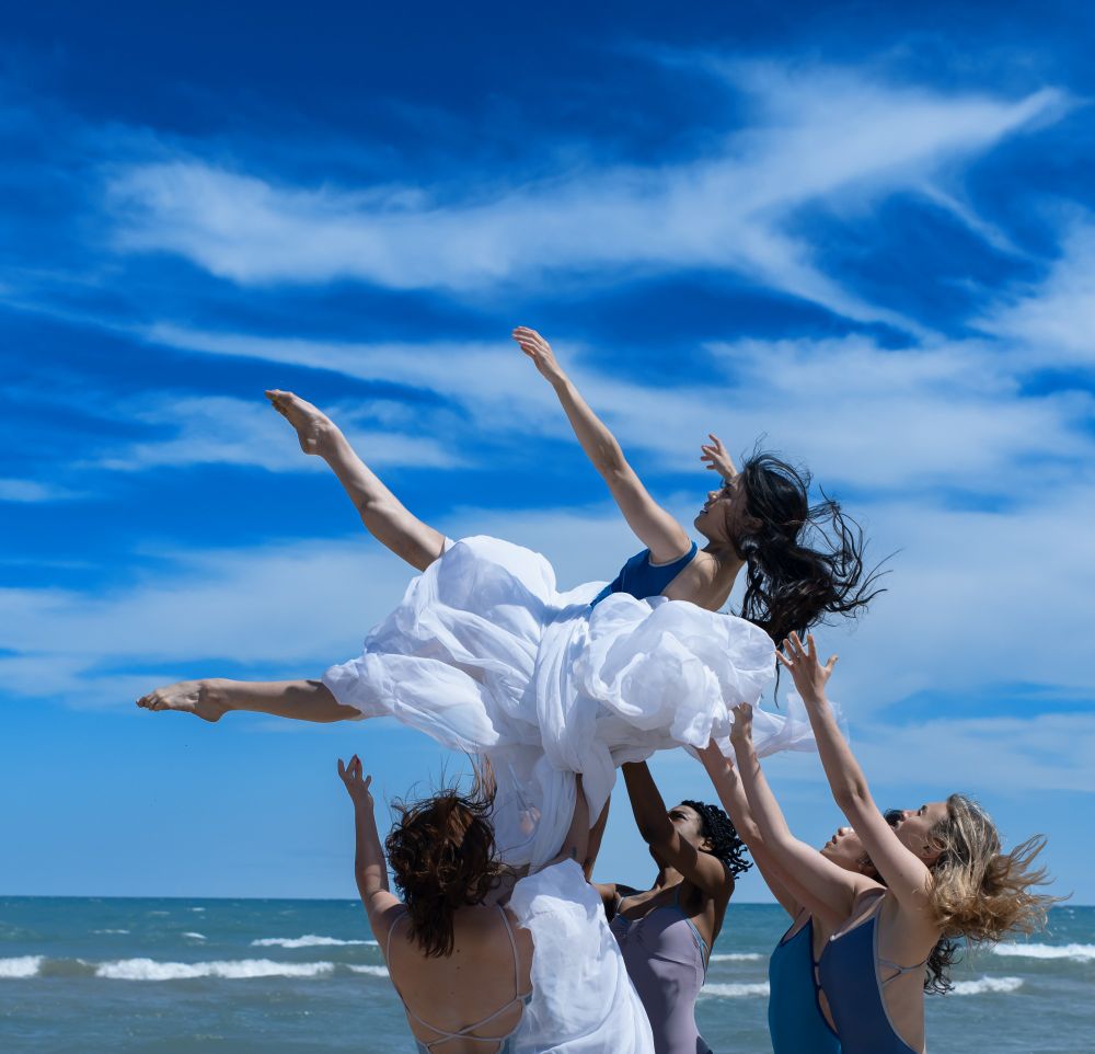 A group of dancers caught a dancer wrapped in white cloth in front of Lake Michigan.
