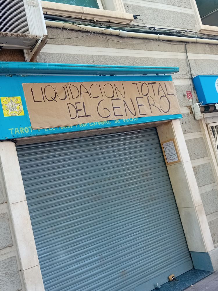 Foto de una tienda con el letrero tapado por un cartel escrito a mano que dice: LIQUIDACIÓN TOTAL DEL GÉNERO 