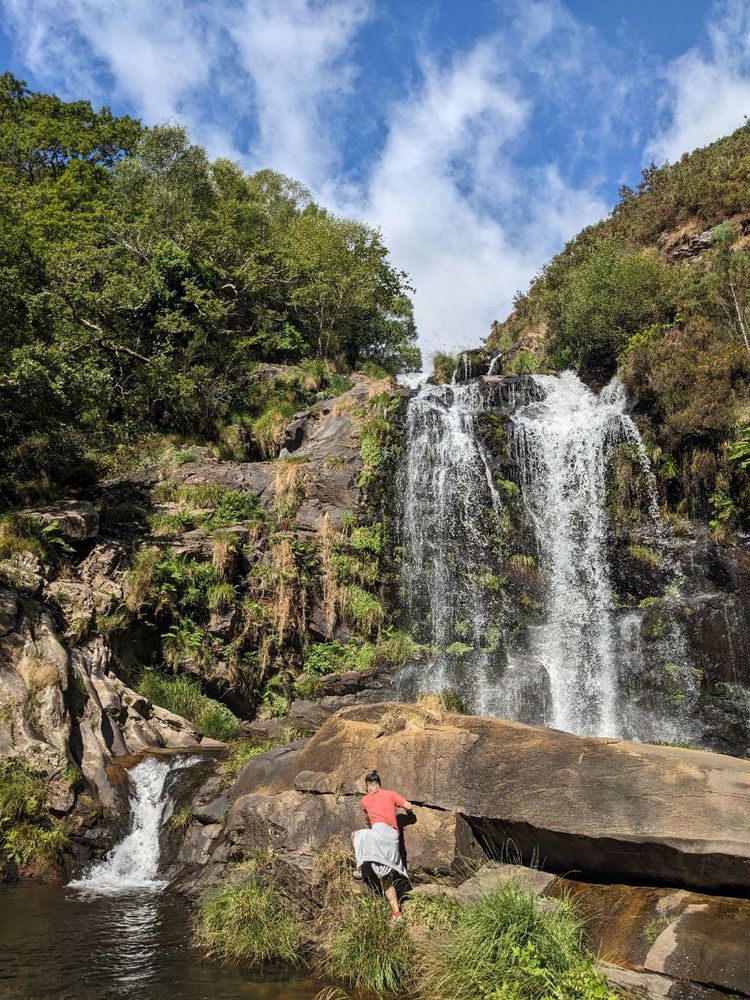 H trepando una roca frente a una cascada en un lago de montaña.