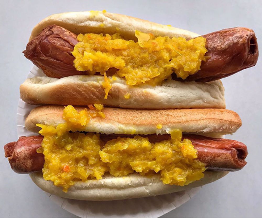 Two hot dogs, fried, placed in a bun, with a yellow relish on it.