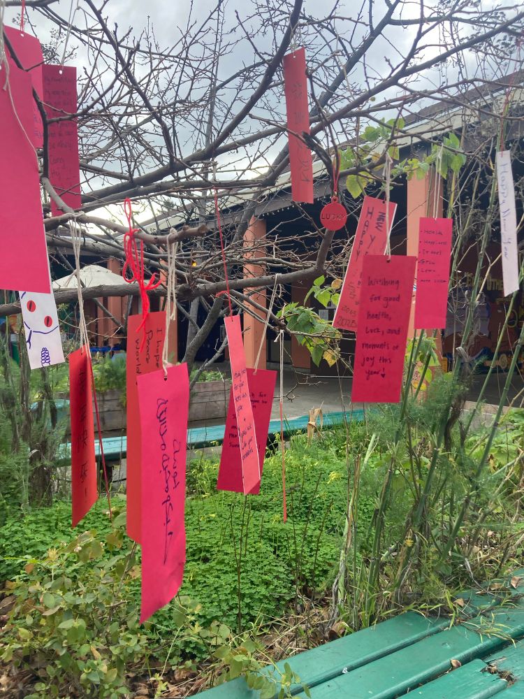 Red ribbons hanging on trees with words in different languages wishing a happy new year.
