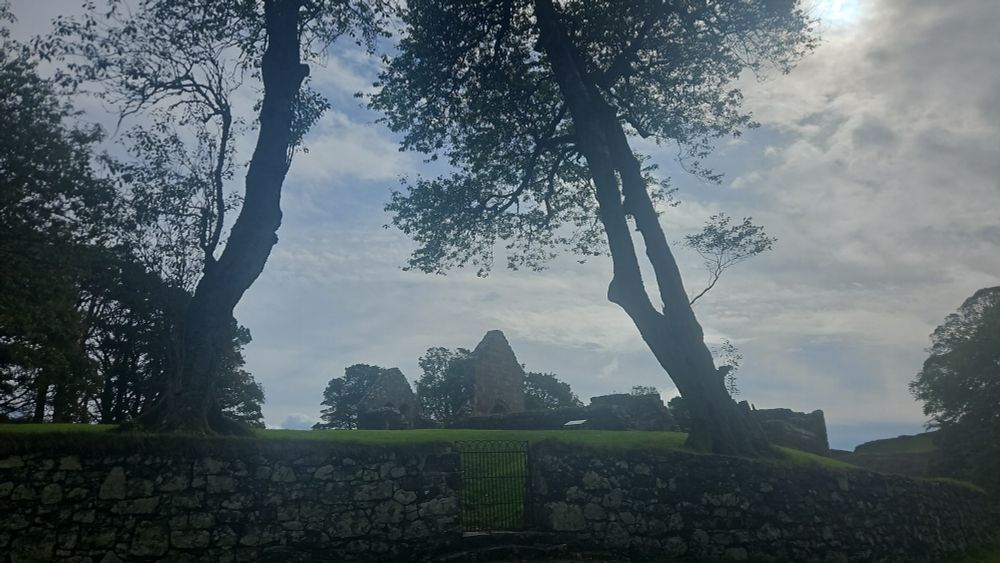 A small raised ruined church seen between two trees.