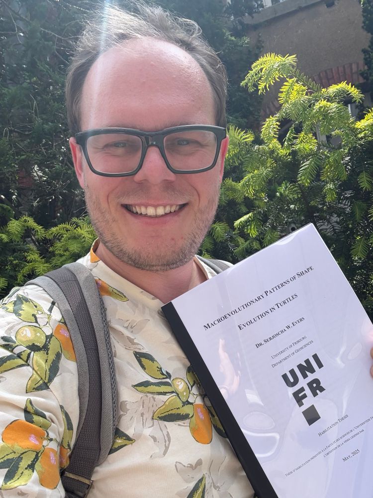 Portrait of myself, smiling with my habilitation document in hand in front of a tree