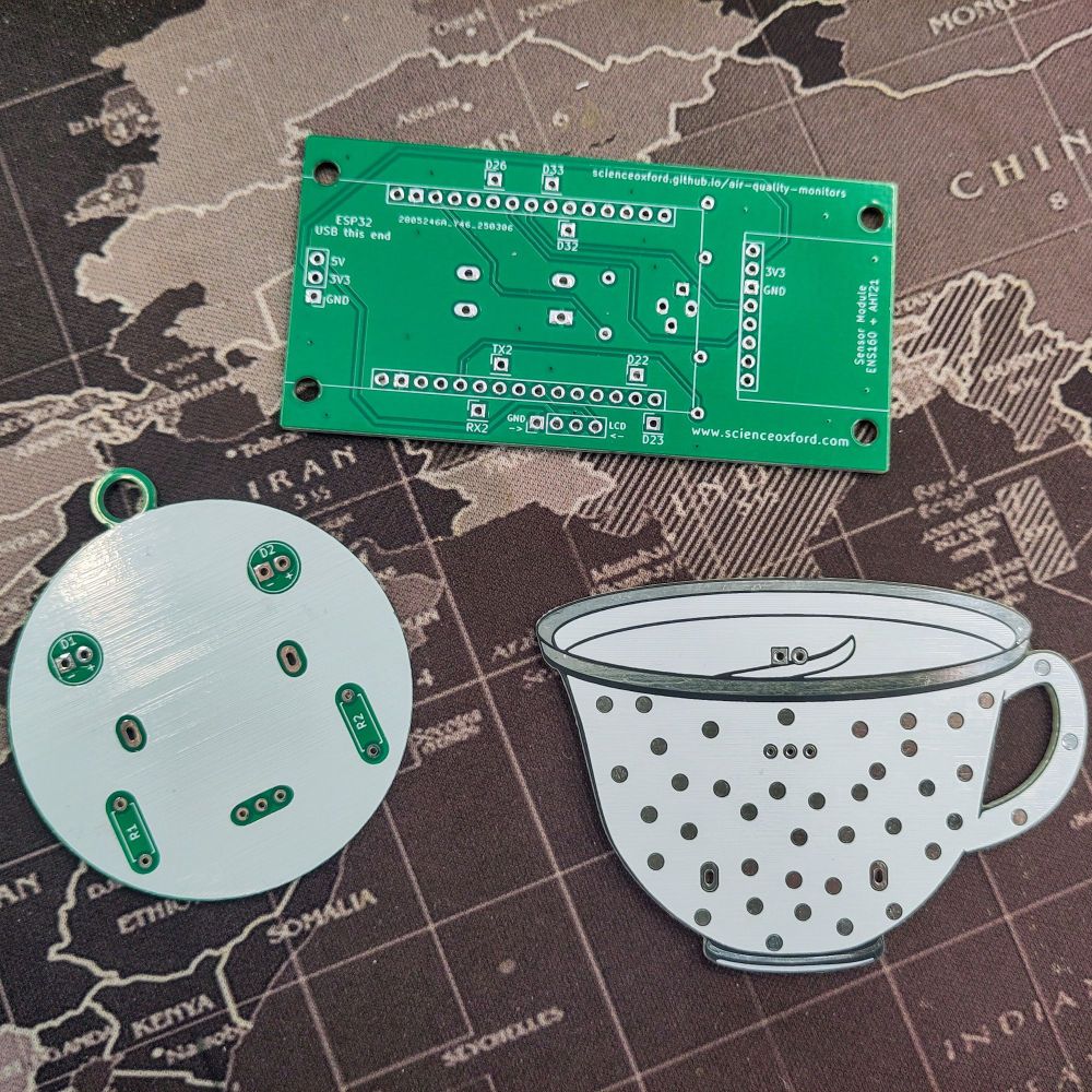 Three printed circuit boards. Top - air quality monitor breakout board. Left - round board with component holes placed as a face. Right - teacup shaped board with silver spots.