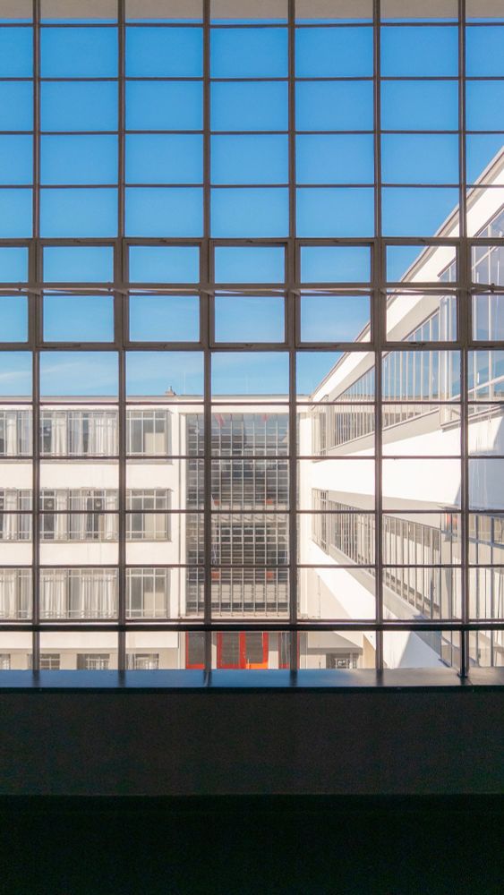 View of a large, grid-patterned window overlooking Bauhaus, seen from the top of a stairway with orange railing accents.