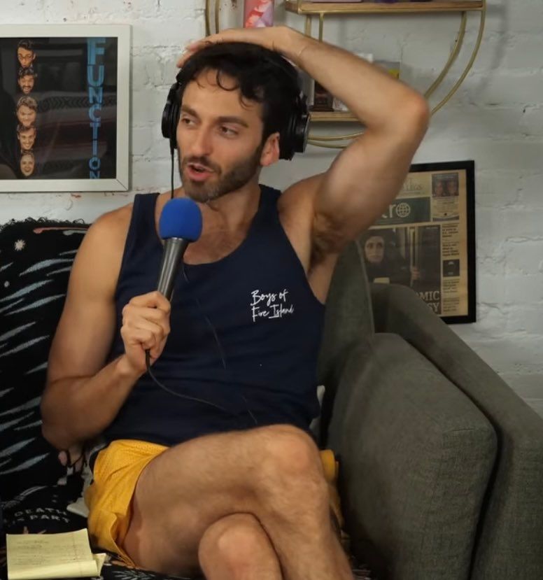 foto do comediante gianmarco soresi sentado em um sofá de pernas cruzadas e com o braço esquerdo elevado até a cabeça, deixando seu suvaco delicioso a mostra