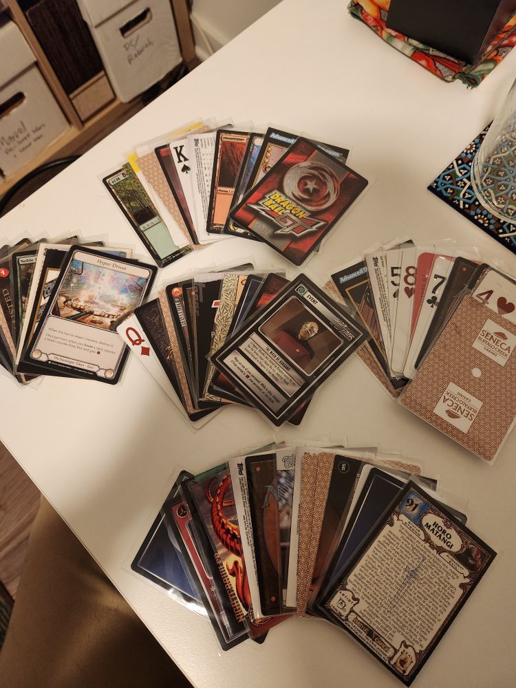 Cards of all kinds fanned out on a table: playing cards, trading cards, train tickets, and trading game cards from several games.