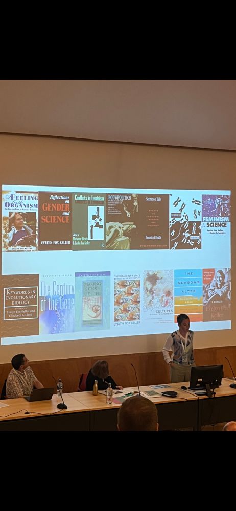 A woman standing before a presentation of books. The woman is Francesca Merlin, the books are by Evelyn Fox Keller. 