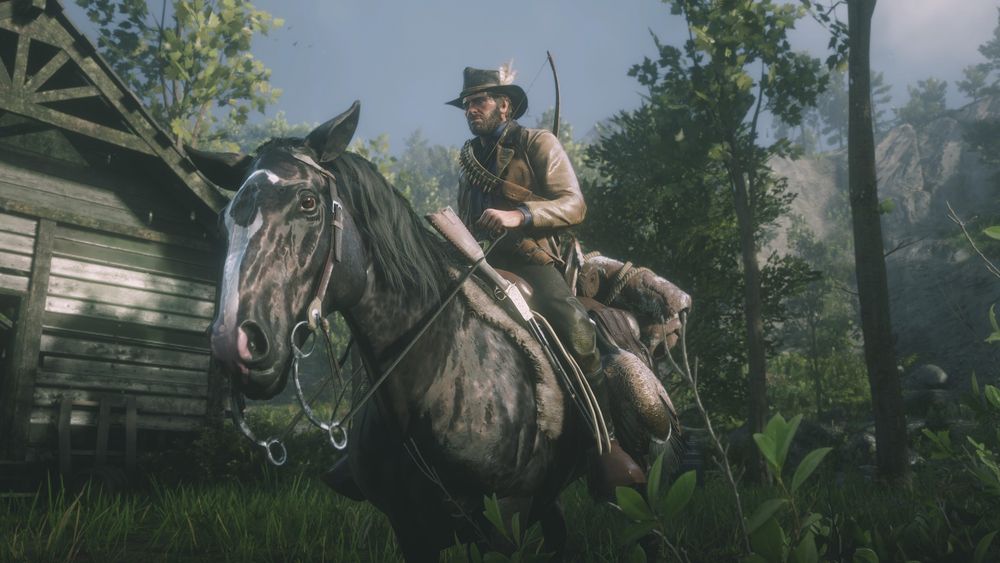 A close up of Arthur sitting atop his horse outside of an abandoned cabin in a forest. The horse looks partially towards the camera.