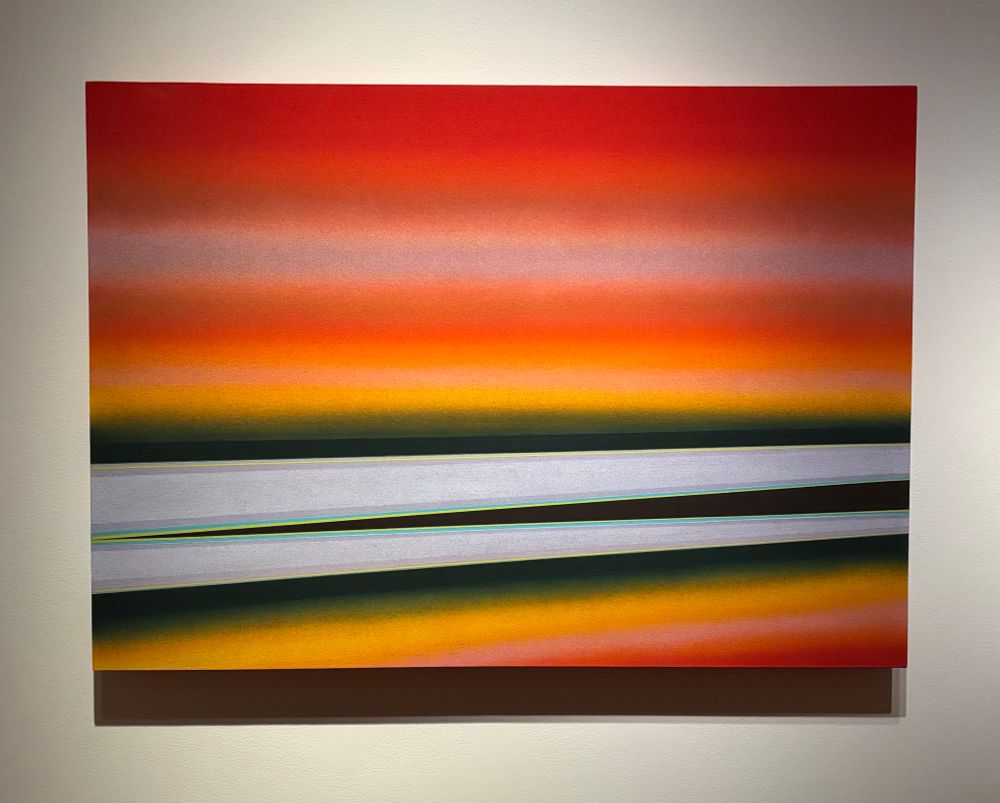 An abstract painting with bright red, orange, yellow, fuzzy horizontal stripes and sharper dark green, black and silver  horizontal geometric “streak” areas across the lower half. It resembles a landscape. 

RITA LETENDRE
Tabori
1976
acrylic on canvas