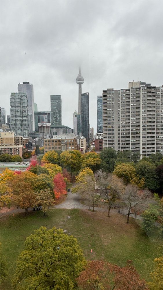 The view of downtown Toronto with the top of the CN Tower missing in the clouds, seen from the back of the AGO from Frank Gehry’s spiral staircase on October 30, 2025. It’s overcast but the grass is green and the trees are turning yellow and red. 