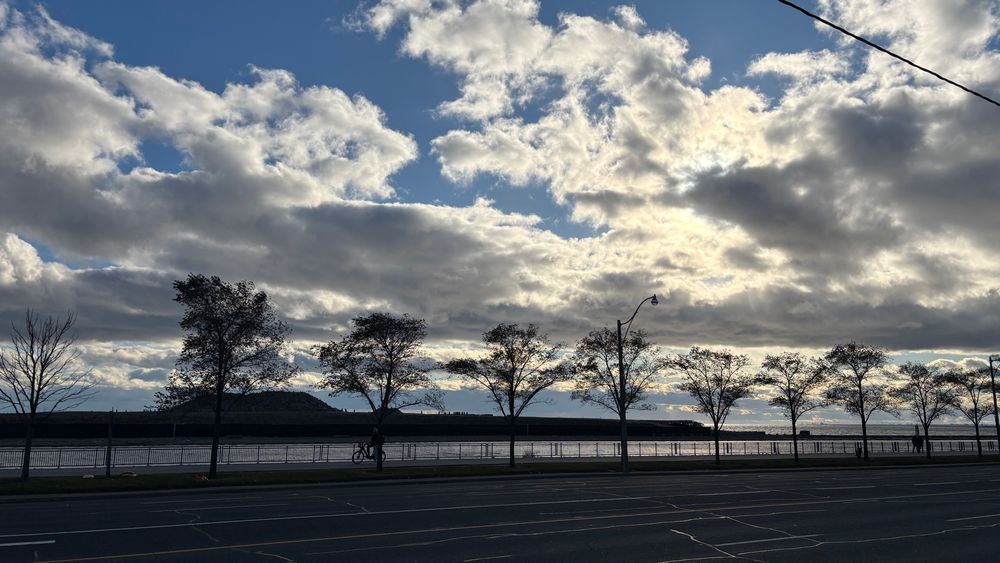 Looking south west to the end of Ontario Place, no trees where they used to be, nothing but razed land jutting out of the lake. Small trees line Lakeshore Blvd, silhouetted against the lake, blue sky and dramatic clouds, backlit by the setting sun. It looks desolate and wrong. Like, something wrong happened here. 