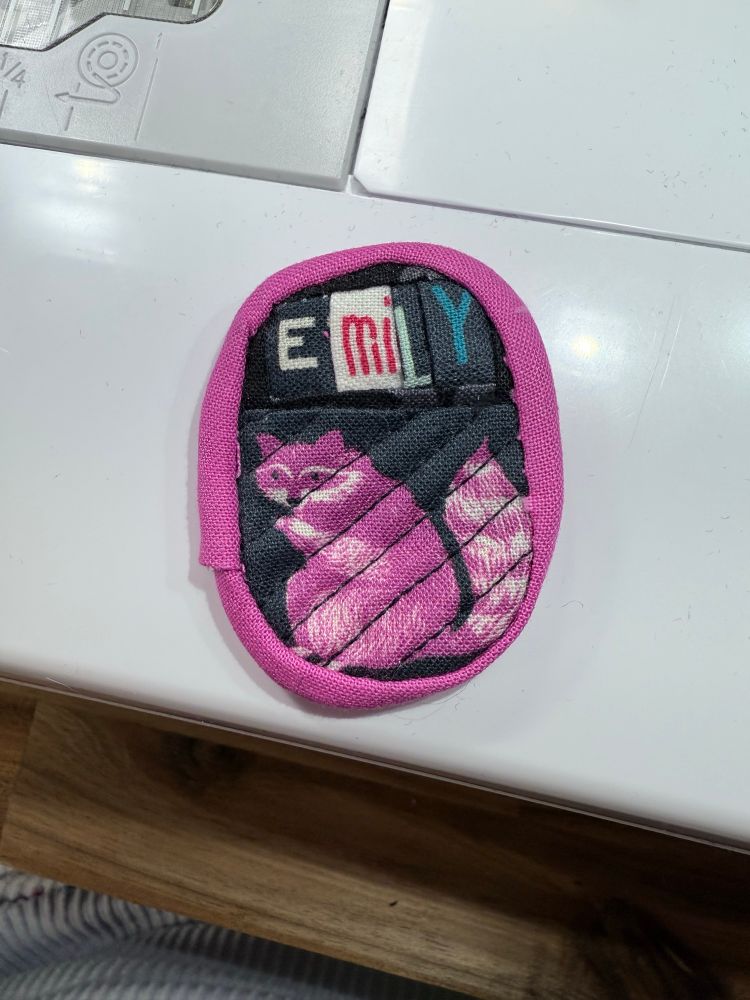 Quilted name tag that says Emily with a raccoon. 