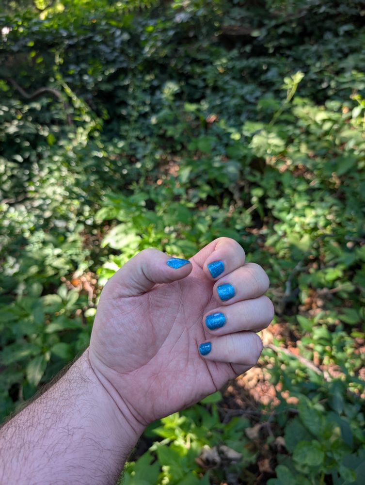 My fisted hand featuring a sparkly lighter blue manicure 