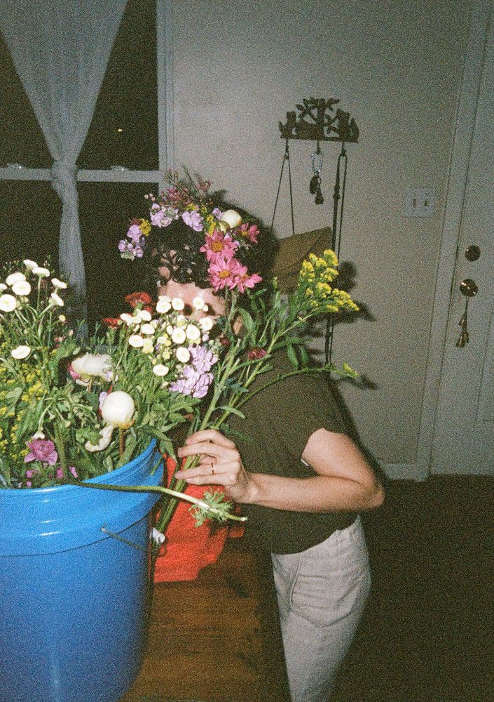A film photo of a woman hiding behind cut flowers. The lighting is dark and somewhat strange.