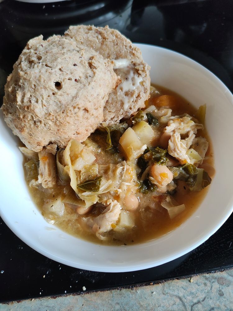 White bowl containing soup with buttered scones on the side 