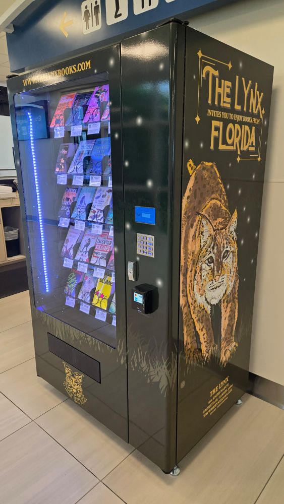 A grwen vending machine containing books. The writing on the side says "The Lynx, Florida"