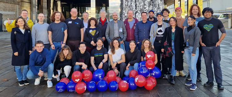 FSFE team and volunteers with red and blue globes, posing outside a building. 