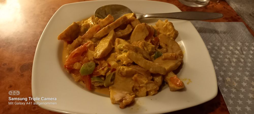 Auf einem weißen tiefen Teller befindet sich eine große Anzahl hähnchenstreifen mit Gemüse in einer gelben Curry Mango Soße