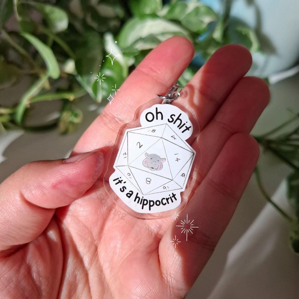 a keychain in the form of a d20. it shows an angry hippo face instead of a 20. around the dice it says "oh shit, it's a hippocrit"